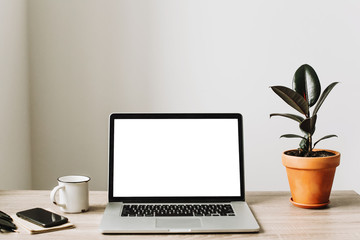 Laptop with empty screen on wooden desktop with phone, notebook, coffee and plant. space for text. mock-up. business workspace. working online home. Freelance concept.