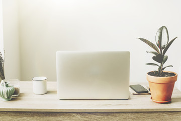 Laptop on wooden desktop with phone, notebook, coffee cup and plant in stylish modern room. Freelance concept. business workspace in home or office. stylish work place. working online