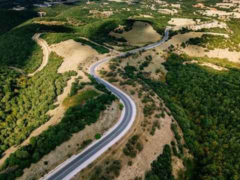 Aerial above view of a rural landscape with a curvy road running through it in Greece. © nblxer