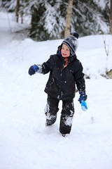 Fototapeta na wymiar Little boy running up the snowy hill with blue shovel