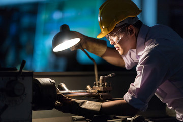 Mechanic Engineer Turner Miller verifies the accuracy of manufacturing steel parts with a scale the size of the measurement device. In the dark room with lamp background. © Nattanon