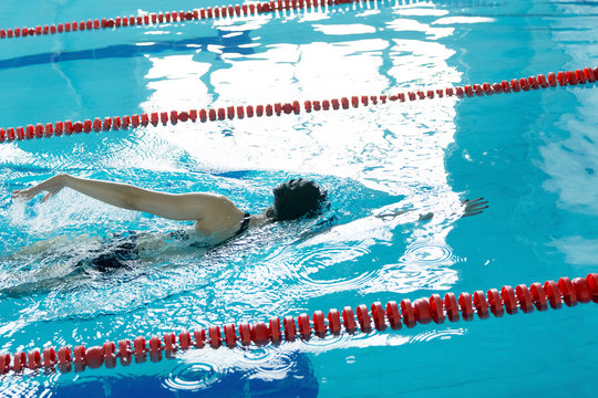 Young girl in goggles and cap swimming crawl stroke style in the blue water pool.