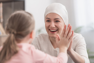 child and sick mother in kerchief holding hands and smiling each other