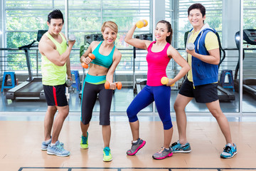 Sportsmen and sportswomen executing functional training routine with dumb-bells in gym