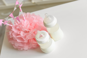 Baby bottles with breast milk with various festive paper decor. It's a girl or baby birthday celebration concept. Baby shower concept. Top view. Free copy space.