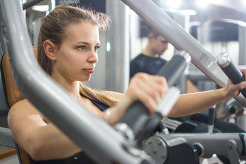 Close up portrait of sporty blonde girl workout on exercise machine in gym.