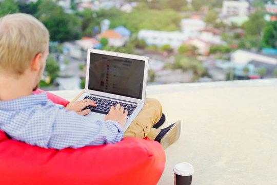 Freelance businessman. Young handsome man working on laptop while sitting on the roof top. Focus on the screen.