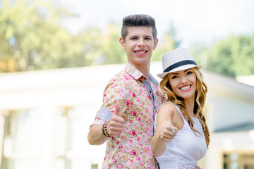 Happy to be together. Beautiful young loving couple showing thumbs up. Outdoors portrait.