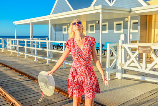 Carefree blonde woman enjoys the sunset light on famous Busselton wooden jetty in Busselton, Western Australia. Australian travel freedom. Female tourist in iconic place.