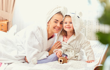 Mother and daughter in bathrobes and towels on the bed in the room. Mothers day.