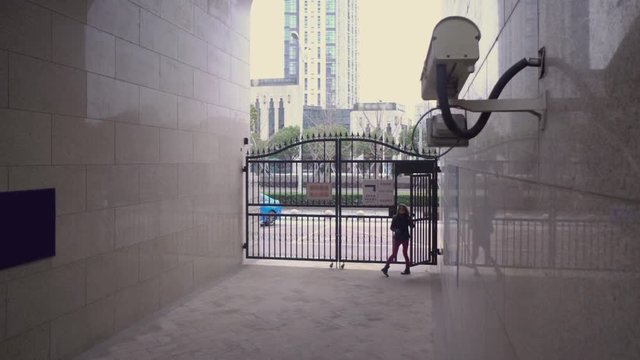 a young girl enters the arch of the house. She's being watched by a security camera.