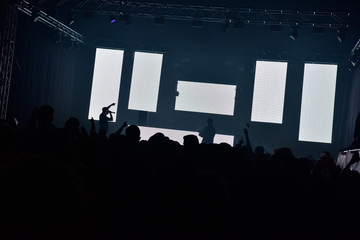 People with hands up during a concert in a hangar. Five led wall ideal to insert text or logos. View of the stage from the dance floor. Silhouette of singer on the stage