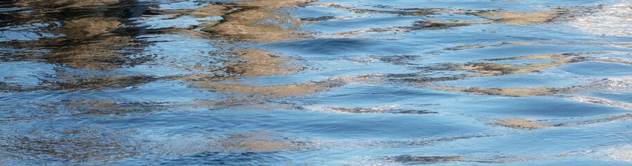 Blue water surface with small ripples or waves and dark reflections as a panoramic banner background with copy space