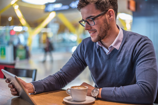 young man at the airport using his tablet and drinking coffee waiting for his flight