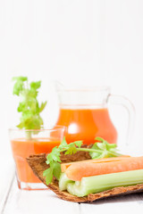 Carrot juice in beautiful glasses, cut carrot and green celery on wood bark bowl on white wooden background. Fresh vegetable drink. Close up photography. Selective focus. Horizontal banner