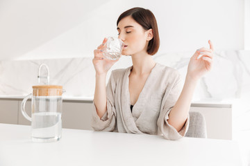 Photo of healthy brunette woman waking up in morning and drinking still fresh water from...