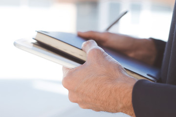 Closeup of young businessman planning with notebook and tablet in his hands