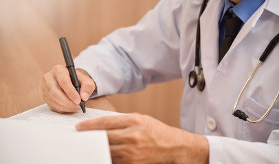 Asian male doctor is writing something on clipboard.