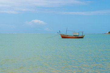 Isolated fishing boat in the middle of the sea with blue sky trapped by an anchor caught on a rope.