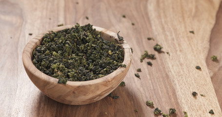 dried green tea leaves falling into wood bowl on table