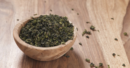 dried green tea leaves falling into wood bowl on table