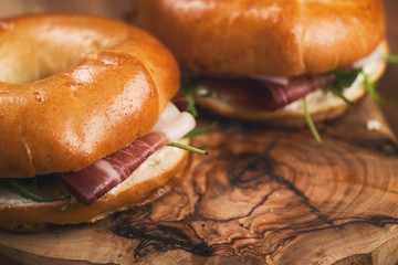 two bagels with prosciutto and cream cheese on wood boar