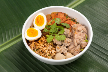 Spicy noodle soup with pork and egg in bowl on banana leaf