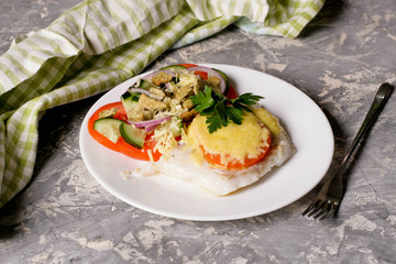 Fish baked with cheese and tomatoes on a white plate