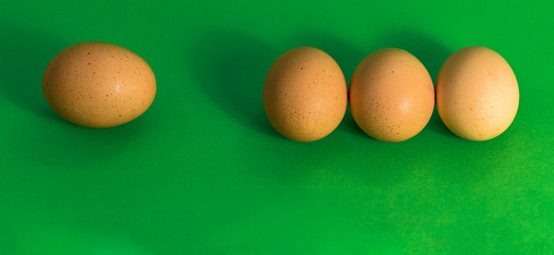 Abstract picture at Easter, three eggs lying close to each other and a single sad egg further away, on grass-green background