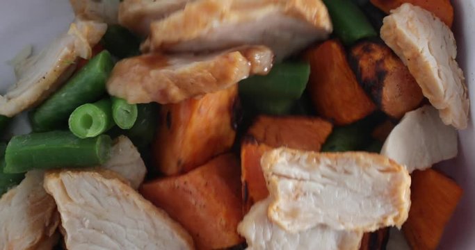 Close video of a roasted turkey, sweet potato and green bean microwaved TV dinner being stirred with a white plastic fork.