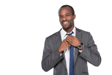 portrait of cheerful african american businessman tying bow tie isolated on white