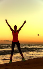 Fototapeta premium Silhouette of fit woman in sports gear on beach rejoicing