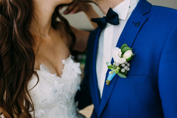 Close-up image of a Boutonniere on the groom's jacket. Blurred bride and groom are kissing. Artwork