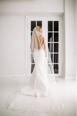 Wedding. Bride in a beautiful dress indoors in a white studio, like at home. The fashionable wedding style is taken in full length. Young attractive blond model with curly hair, like a bride