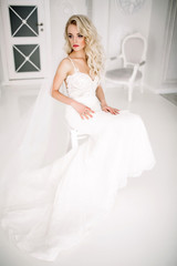 Wedding. Bride in a beautiful dress indoors in a white studio, like at home. The fashionable wedding style is taken in full length. Young attractive blond model with curly hair, like a bride