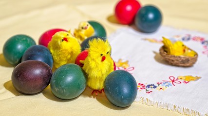 Colorful handmade Easter eggs in the company of traditional small yellow chickens on the embroidered napkin.
