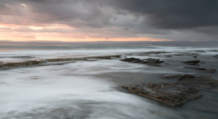 Rocky seashore seascape with wavy ocean during sunset