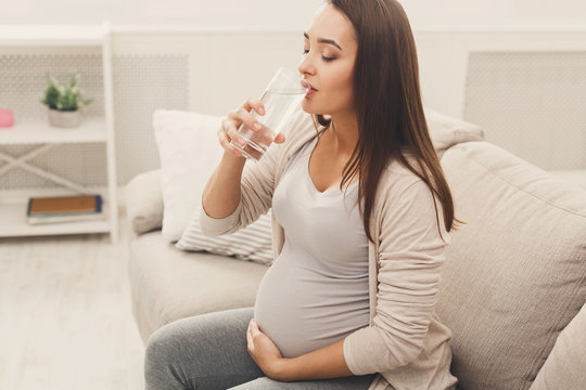 Pregnant woman drinking water sitting on sofa