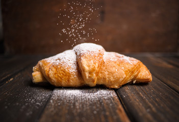 croissant with powdered sugar on wooden desk