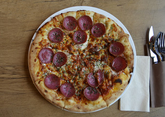 A yummy but unhealthy fast food pizza with salami, cheese, tomato sauce, herbs and crispy crust