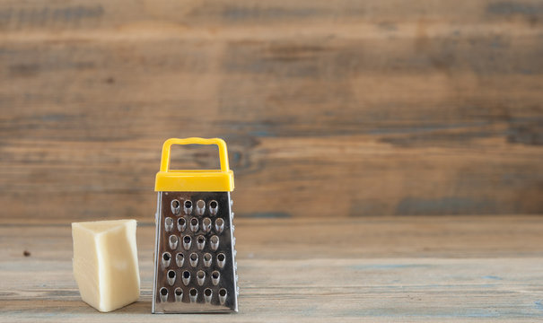 steel grater and cheese on wooden board
