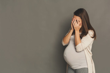 Crying pregnant woman, gray studio background