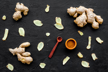 Seasoning. Ground ginger in small bowl near sliced ginger root on black background top view