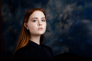 Portrait of a young long hair girl looking at the camera on dark blue blurred background