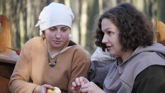 Close-up of viking woman knitting and talking with other woman in a forest camp