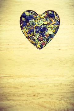 Dried herb leaves heart shaped on wooden surface