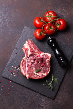 Raw rib eye steak with spices on black slate plate. Dark background.