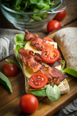 Ciabatta sandwich with arugula salad, bacon and yellow cheese.