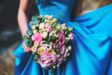 A girl in a blue dress is holding a wedding bouquet of flowers from roses