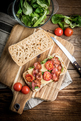 Ciabatta sandwich with arugula salad, bacon and yellow cheese.